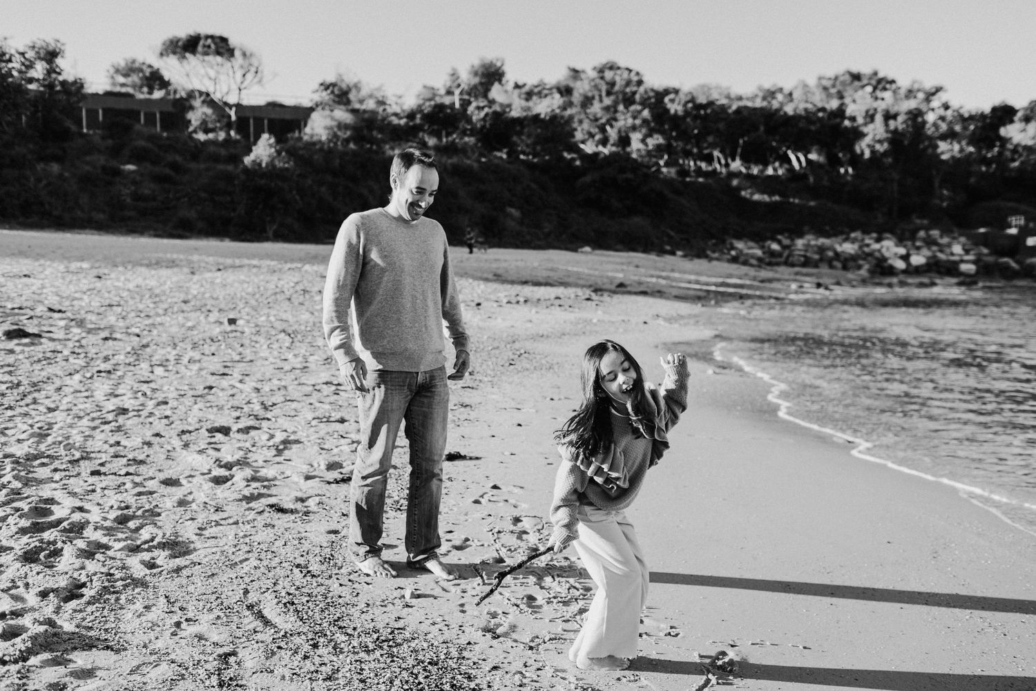 Black and white photo of a father and daughter playing on a beach shoreline.