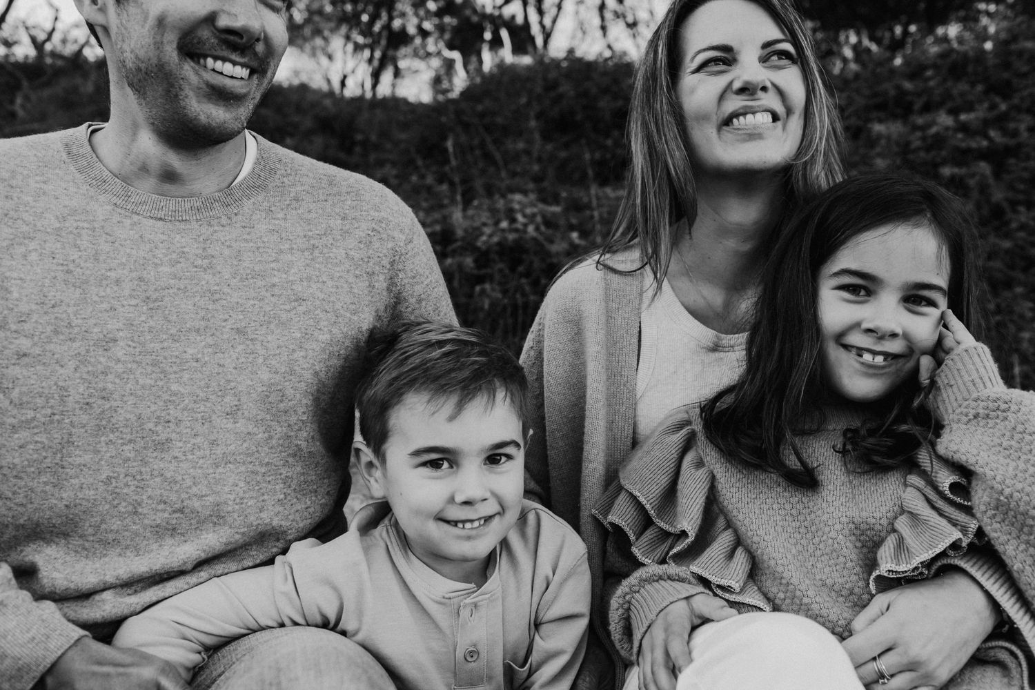 Black and white close-up of a joyful family of four laughing together outdoors.