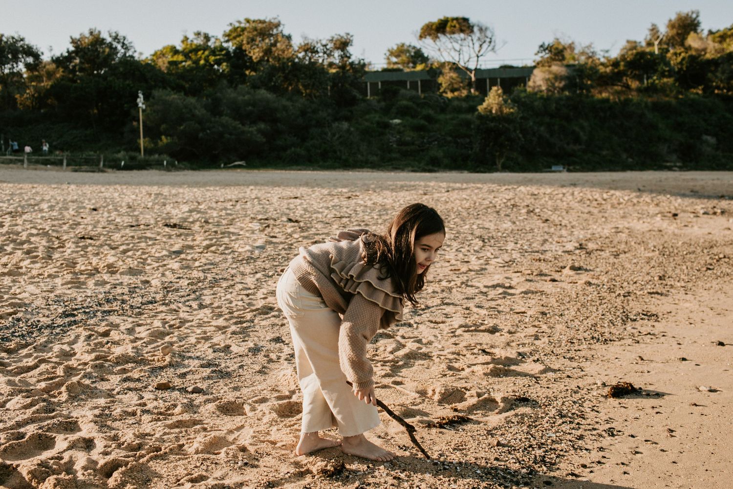 Young girl bending down to draw in the sand on a sunny beach.