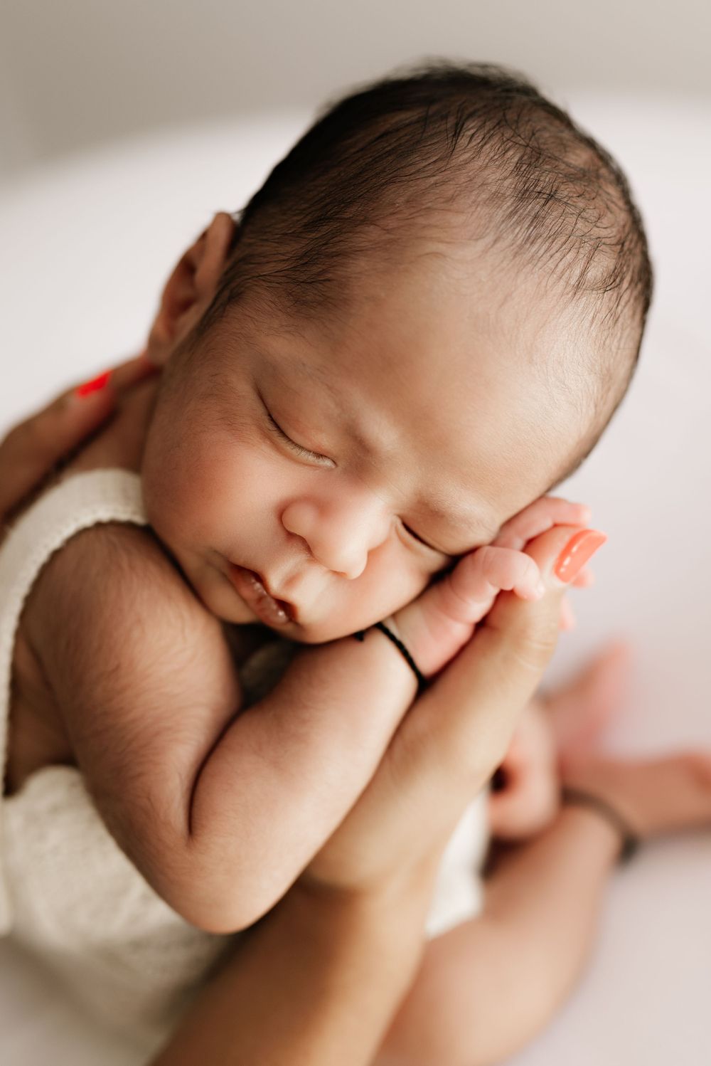 Sleeping newborn baby peacefully resting in soft blanket with hands curled up near face.