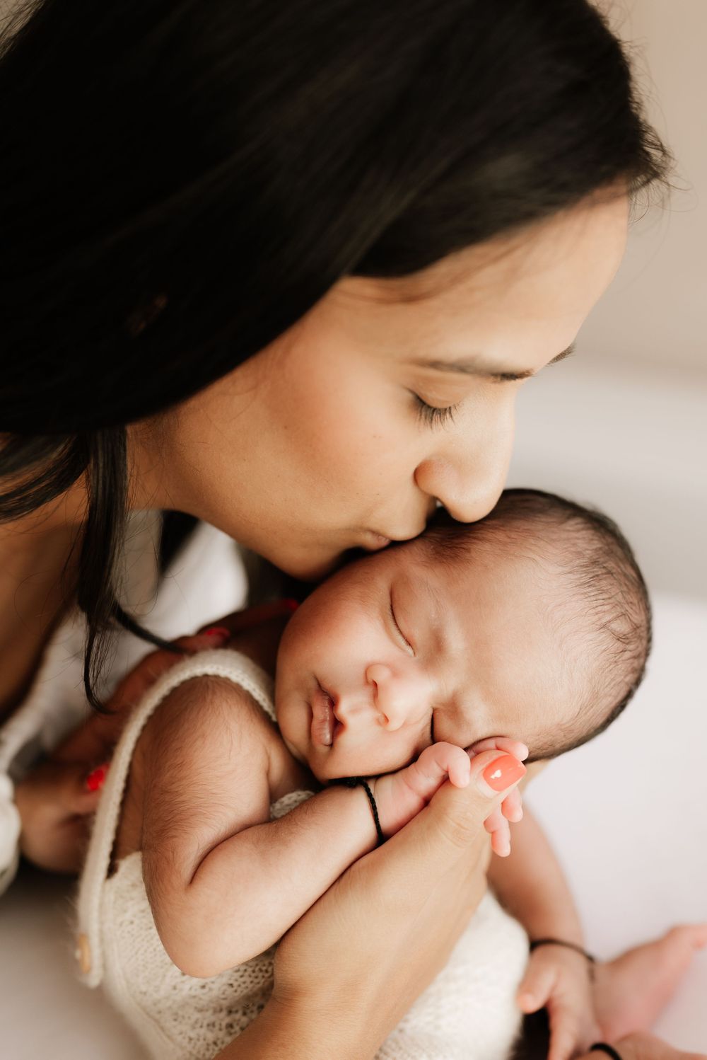 Tender moment of parent gently kissing sleeping newborn's head.