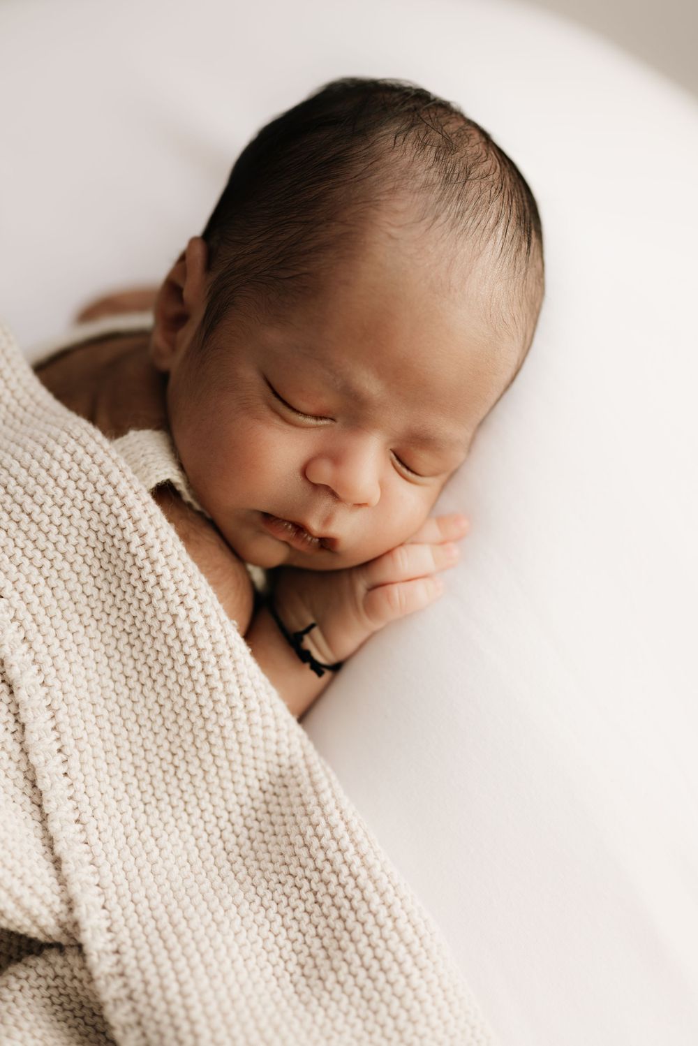 Sleeping newborn wrapped in cozy knit blanket during studio photoshoot.