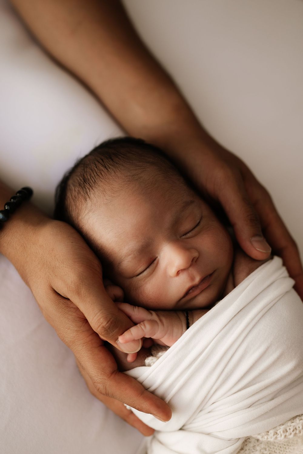 Sleeping newborn wrapped in white fabric held gently in caring hands.