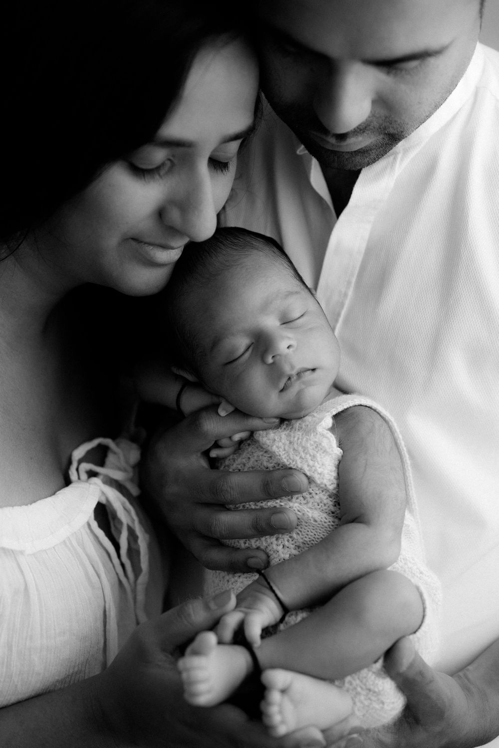 Black and white portrait of new family tenderly holding sleeping infant.