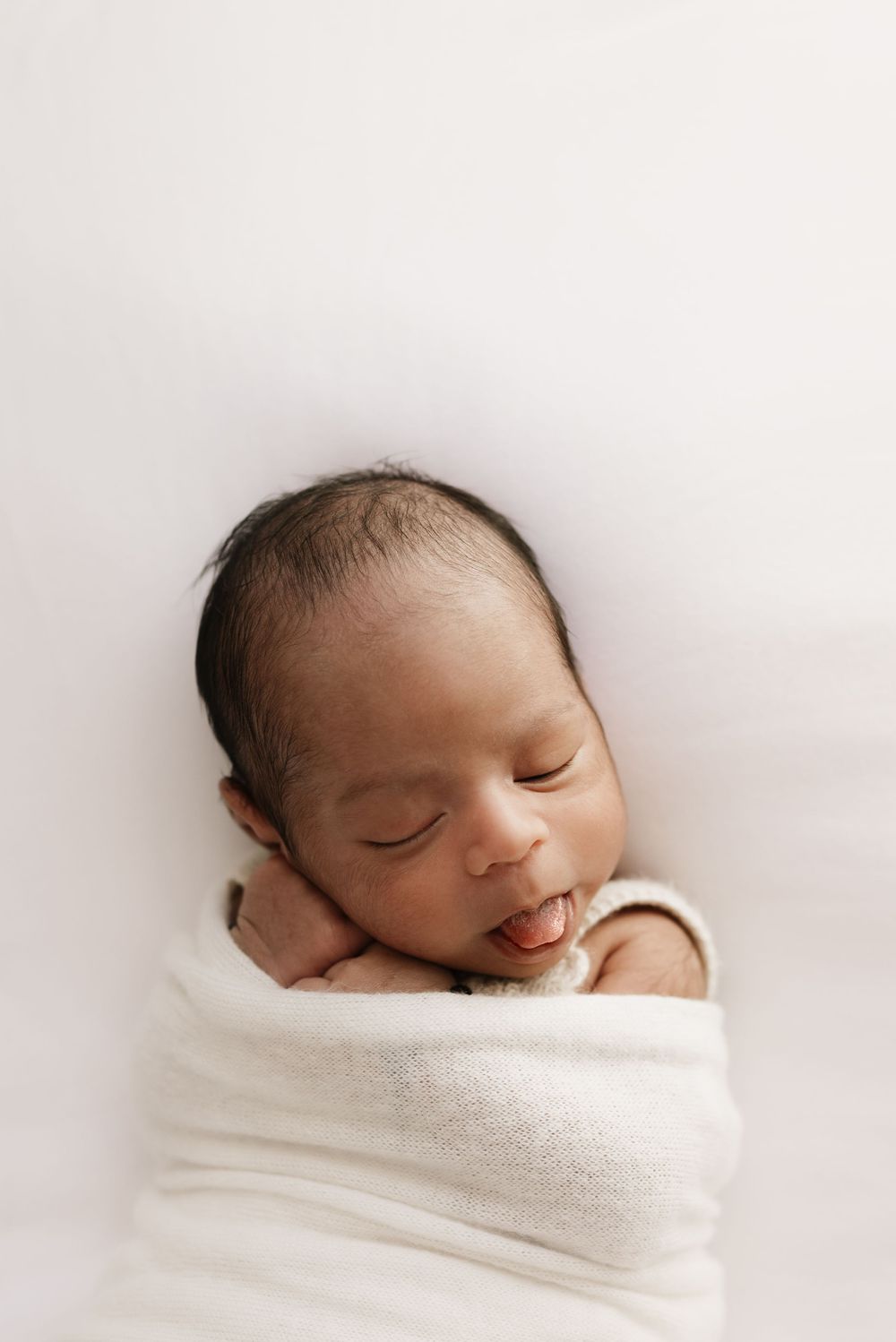 Peaceful sleeping newborn swaddled in white wrap against neutral background.