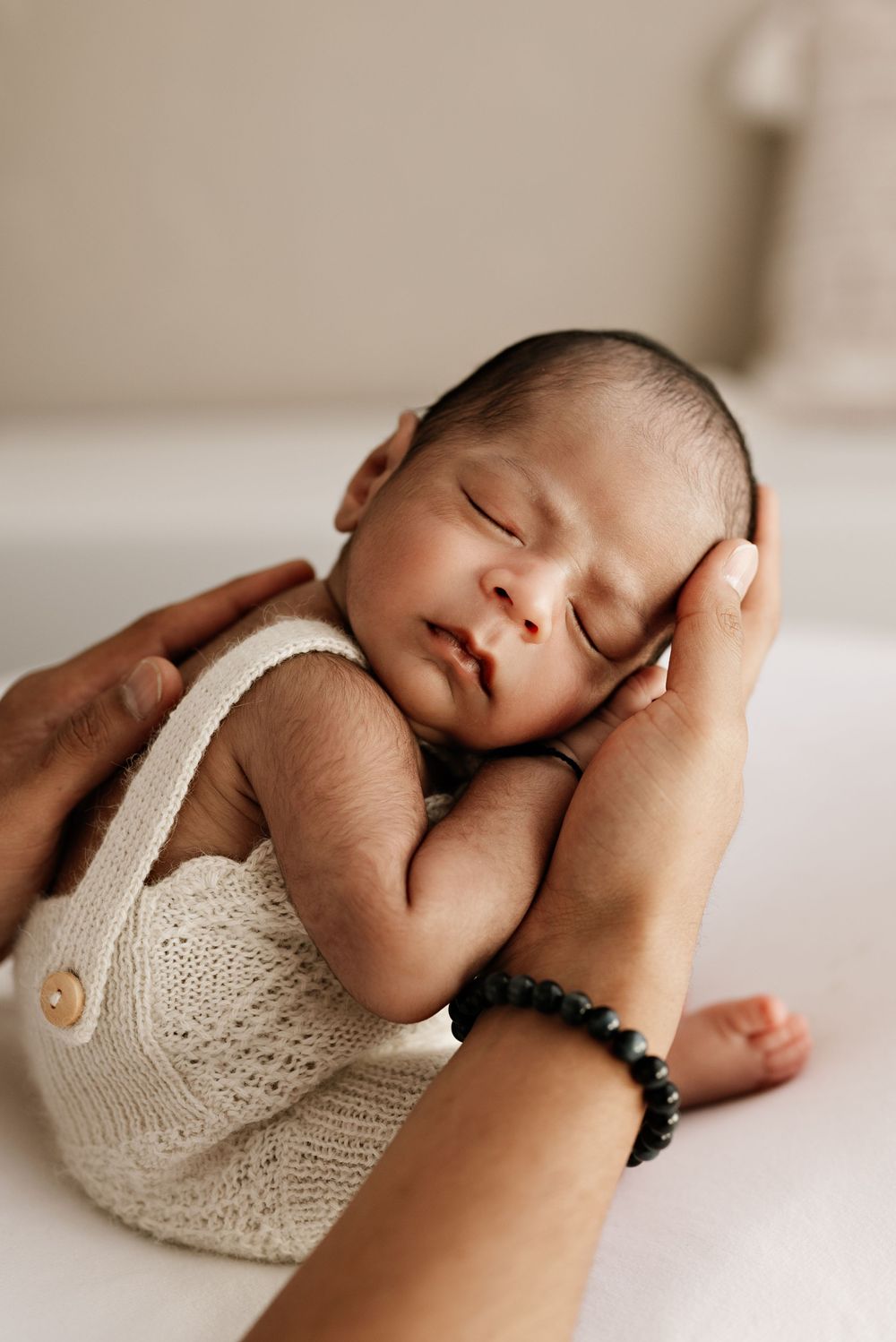 Peaceful sleeping newborn wearing white knit romper cradled in gentle hands.