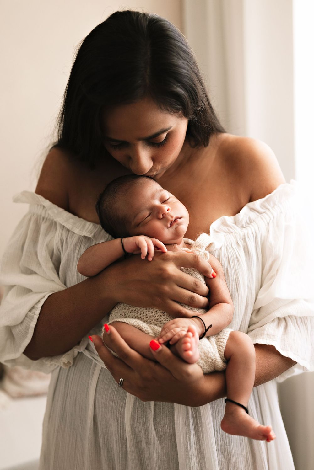 Intimate moment between mother and sleeping newborn in white dress.