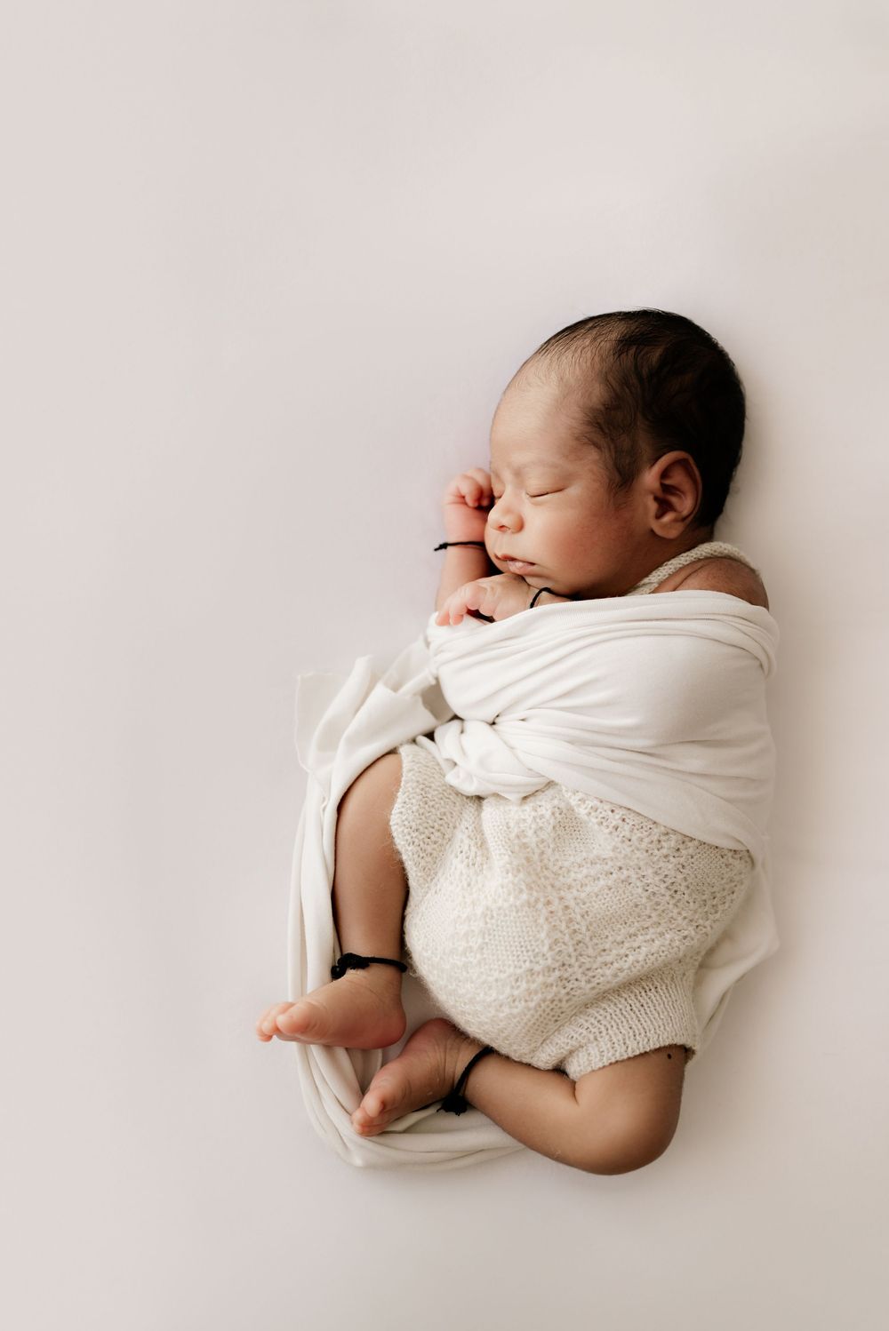 Newborn baby sleeping soundly wrapped in white fabric against light background.