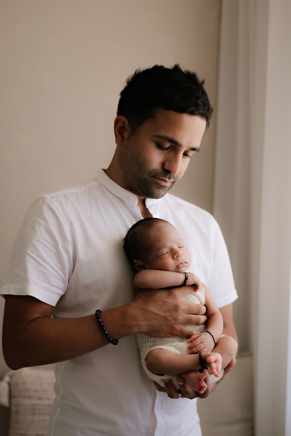 Tender moment between parent holding sleeping newborn in white room.