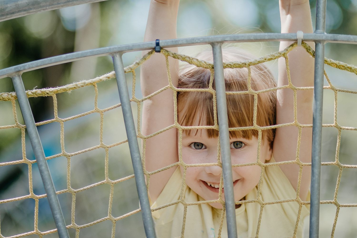 Child peering through playground equipment with a playful expression.