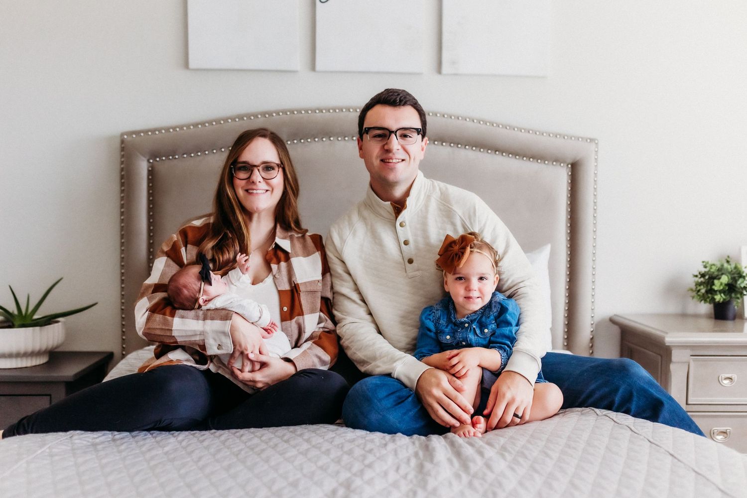 A family relaxing together on a gray upholstered bed in their home.