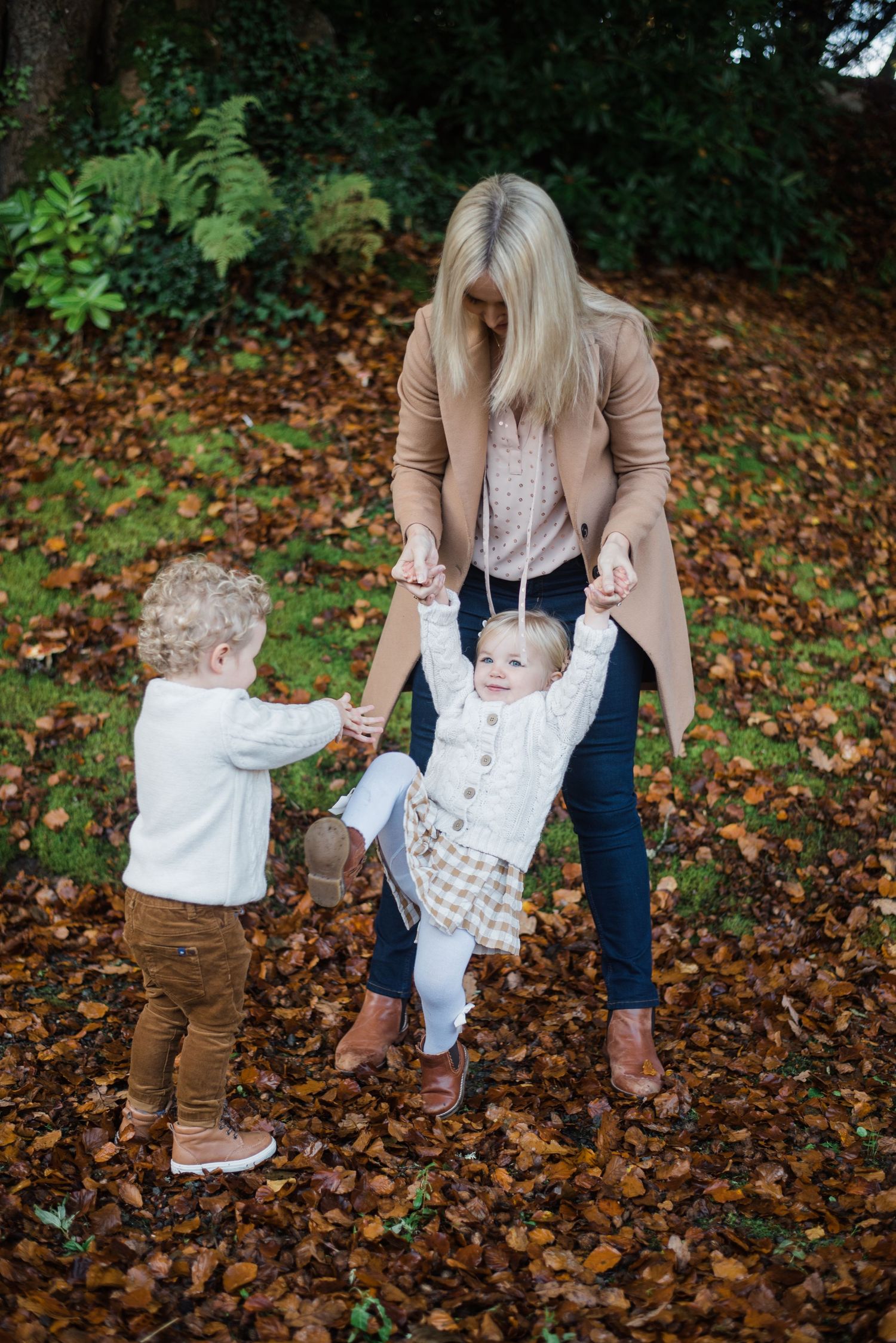 A playful autumn scene of children playing in fallen leaves with an adult in a beige coat.