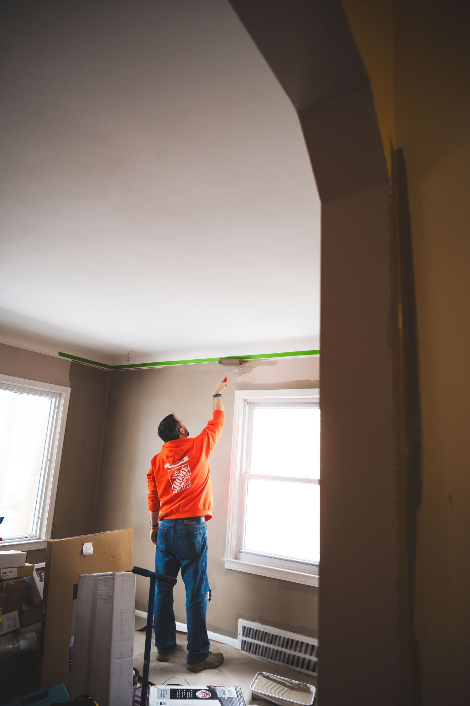 Person in orange sweatshirt painting ceiling while standing on ladder.