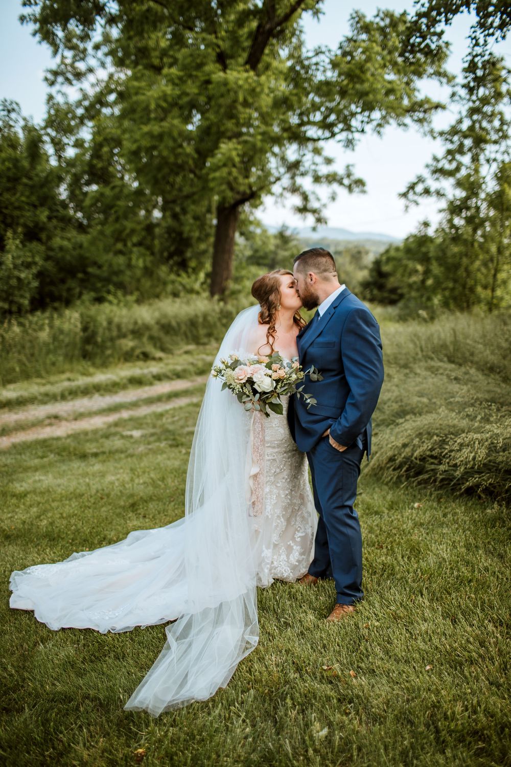 A newlywed couple sharing a tender moment on a grassy path with her flowing white veil.