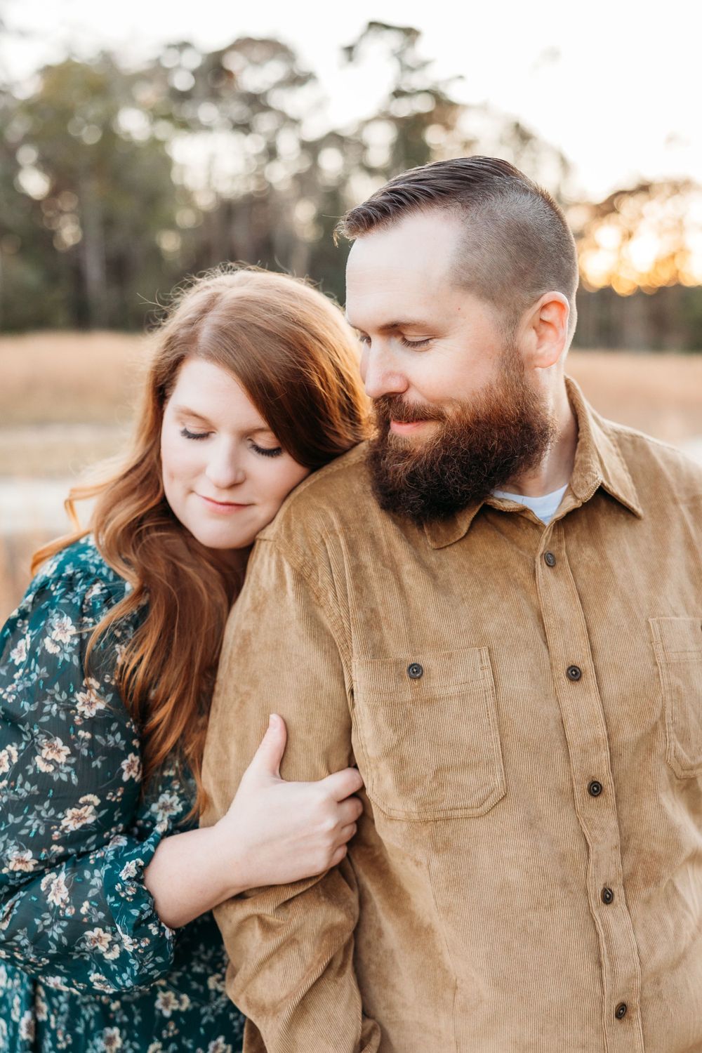 Romantic couple in casual attire share an intimate moment at sunset in a rustic outdoor setting.
