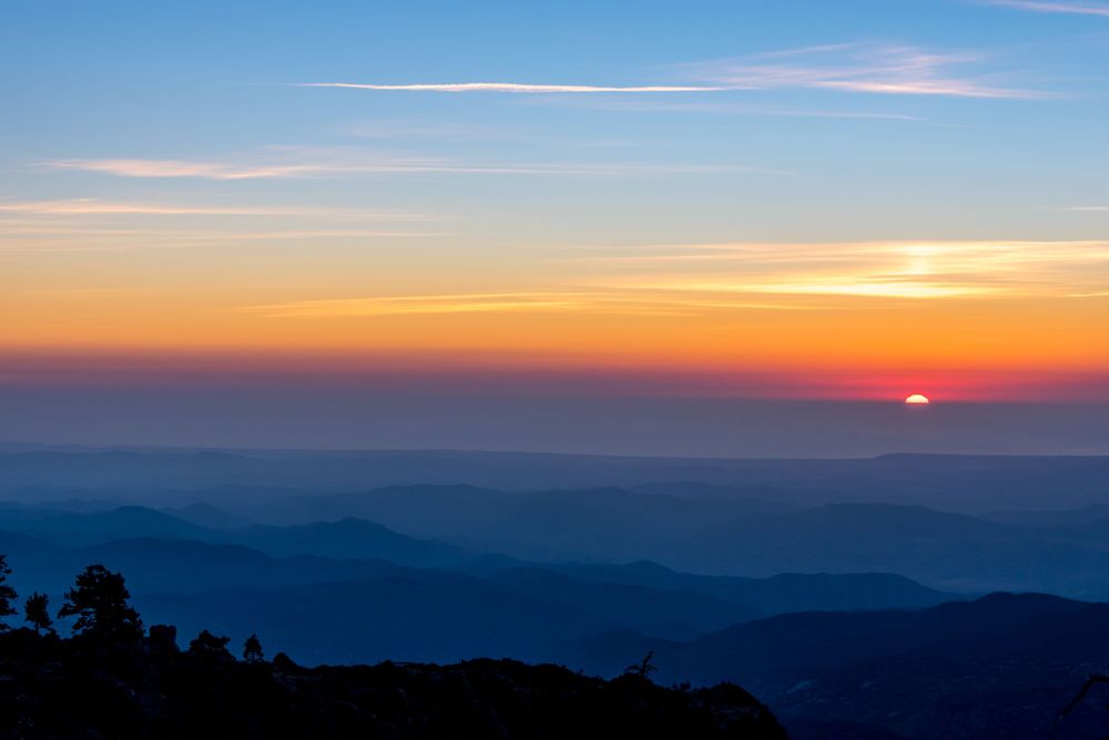 Mountain landscape at dusk with layers of hills silhouetted against an orange and blue sky.