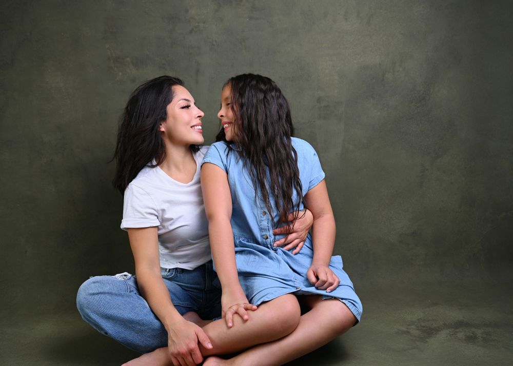 Two people in casual attire share an intimate moment against a textured gray background.