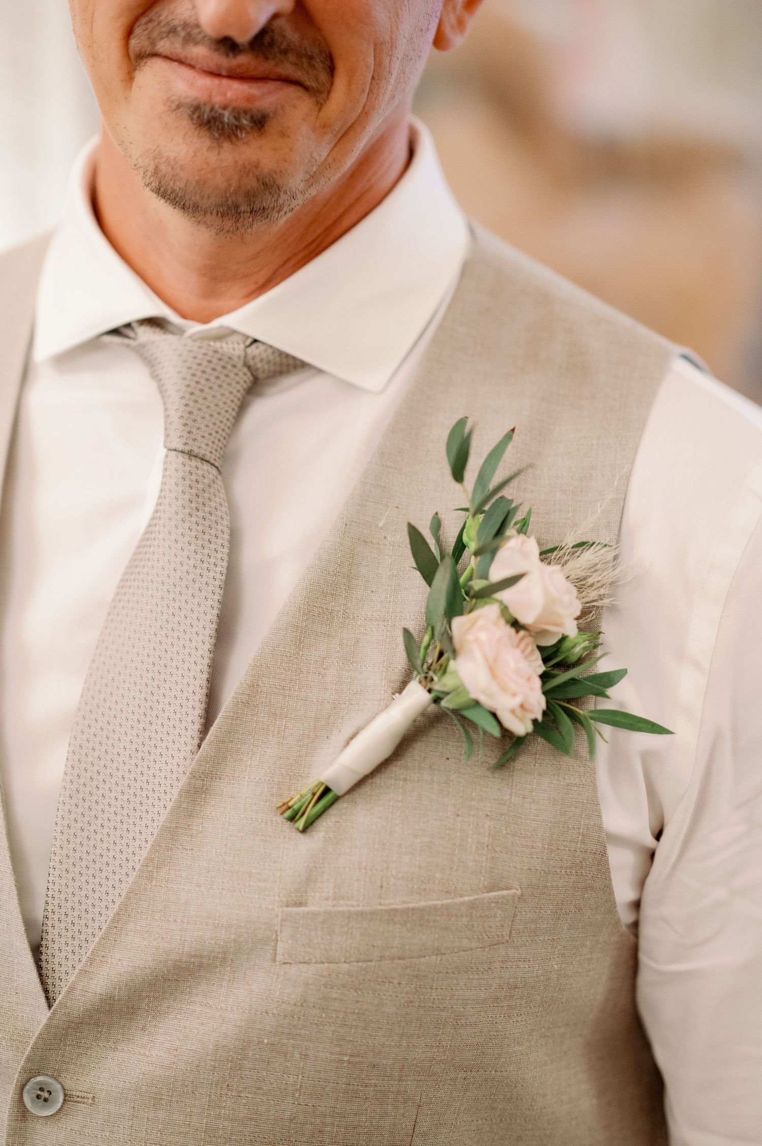 Close-up of a beige vest with a pink and green floral boutonniere and textured tie.