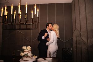 Couple shares kiss by candlelit dessert table with wedding cake.