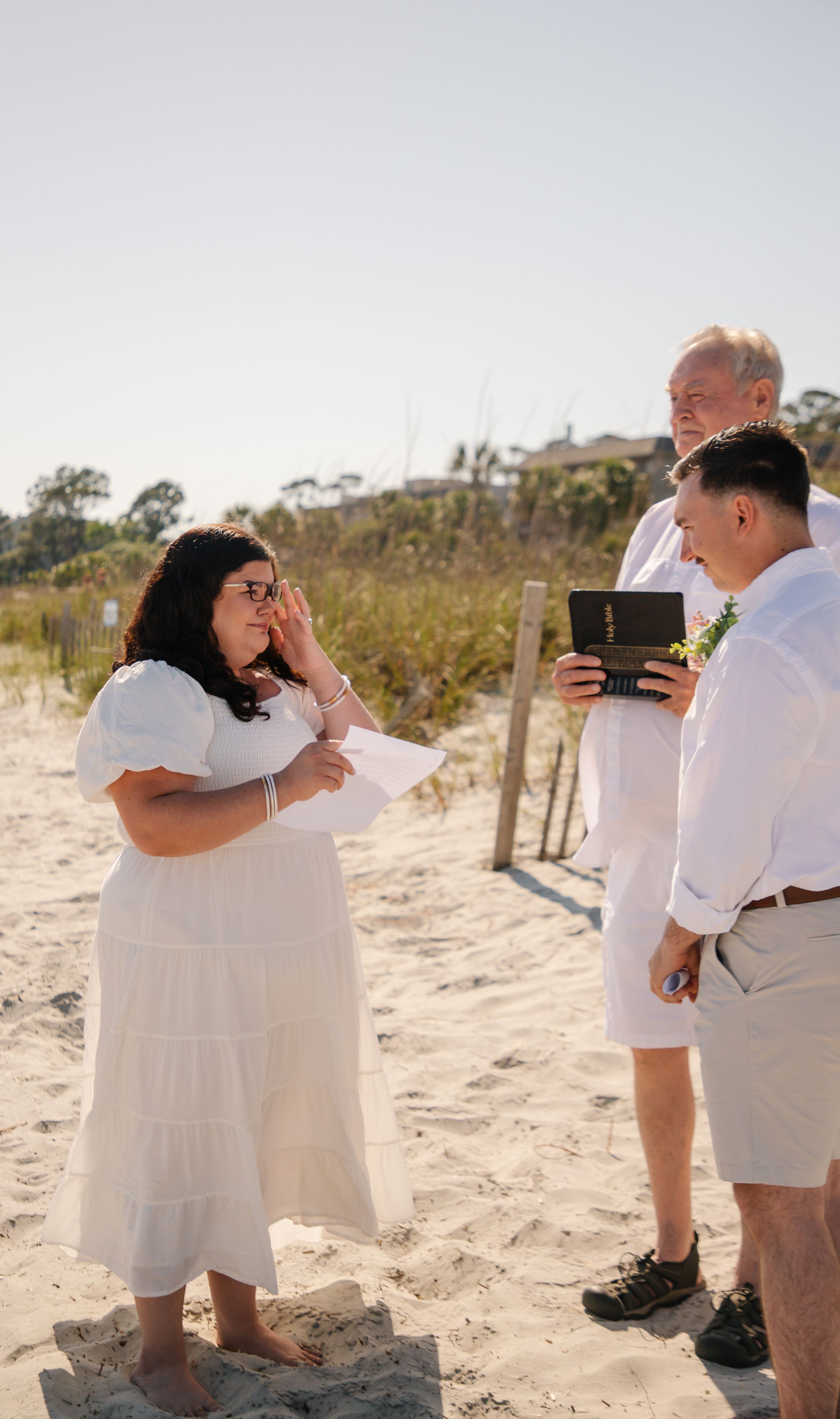 Emotional wedding ceremony on sandy beach with couple and officiant.