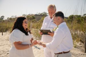 Joyful exchange of rings during beachside wedding ceremony.