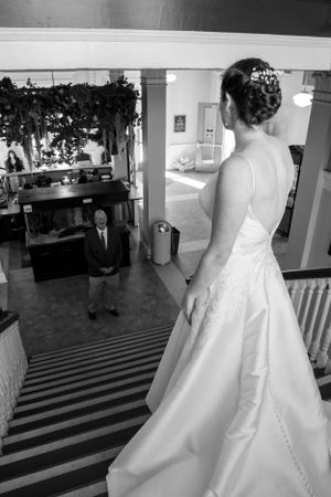 A black and white wedding photo showing a first look moment on stairs with an elegant bridal gown in view.