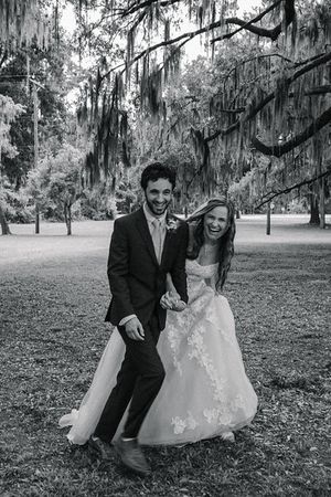 A black and white wedding photo captured under Spanish moss trees in a southern garden setting.