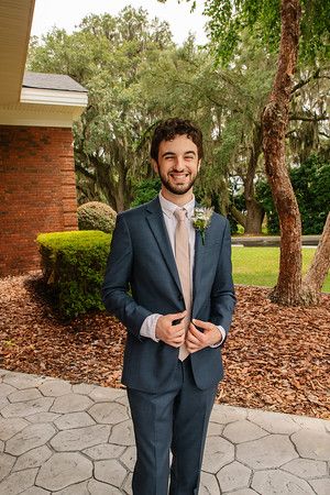 Groom in navy suit and blush tie stands in garden setting with Spanish moss backdrop.