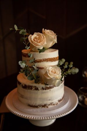 Elegant semi-naked wedding cake decorated with cream roses and eucalyptus.