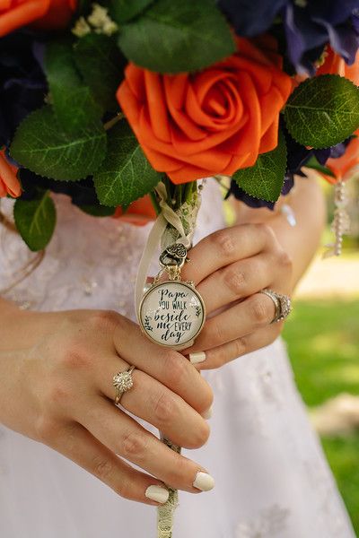 Orange roses in bouquet with sentimental locket charm and wedding rings.