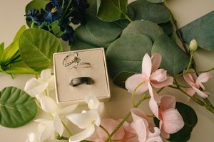 Wedding ring box displayed with delicate pink and white flowers and green foliage.