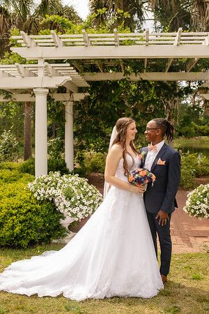 Bride and groom share romantic moment under white pergola in garden setting.