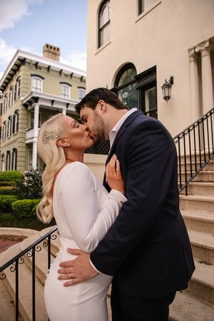 A romantic kiss shared on historic building steps in formal wedding attire.