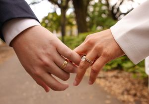 Close-up of newlyweds' hands showing wedding rings against white dress.
