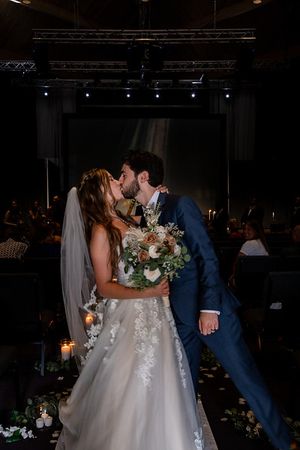 Romantic wedding moment captured in dark venue with dramatic lighting and floral decorations.