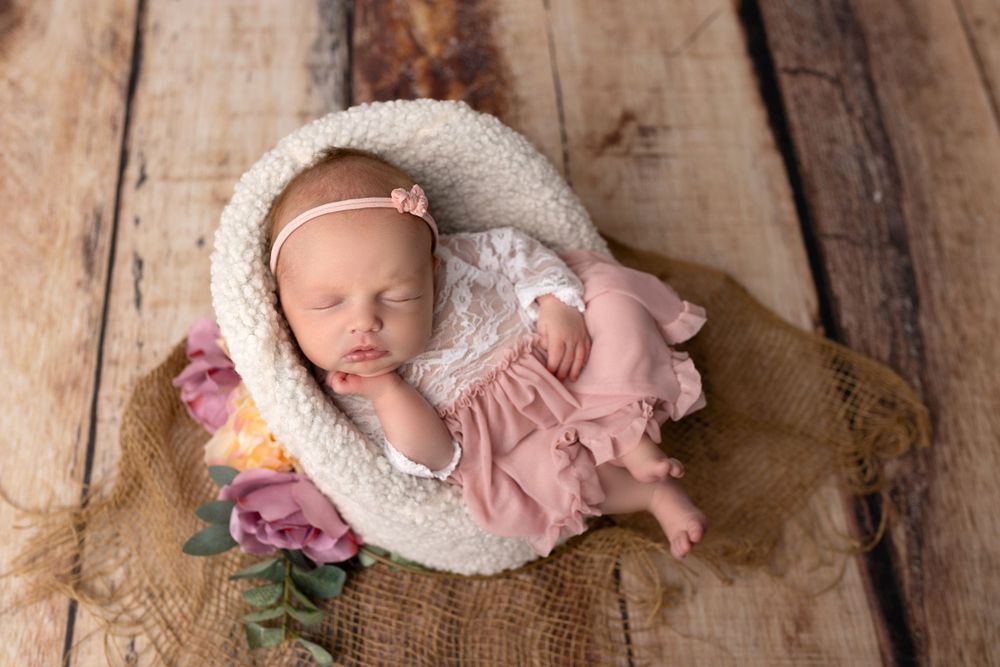 Sleeping newborn in pink dress nestled in cream-colored round cushion with pink flowers.