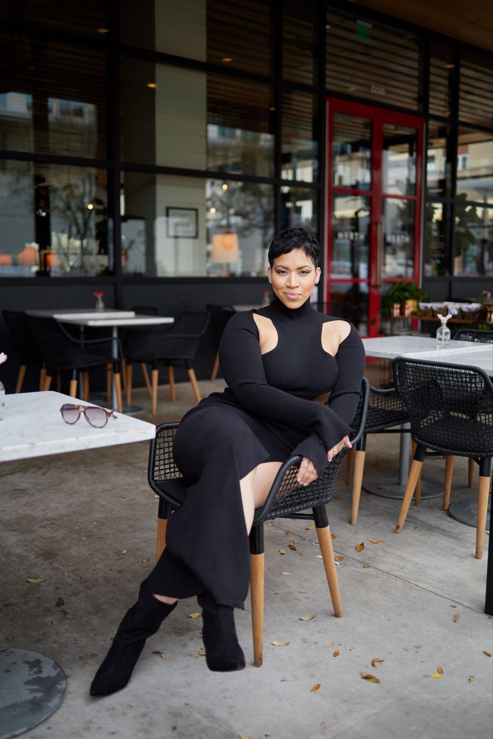 A sleek all-black ensemble with a fitted long sleeve dress and boots at an outdoor cafe setting.