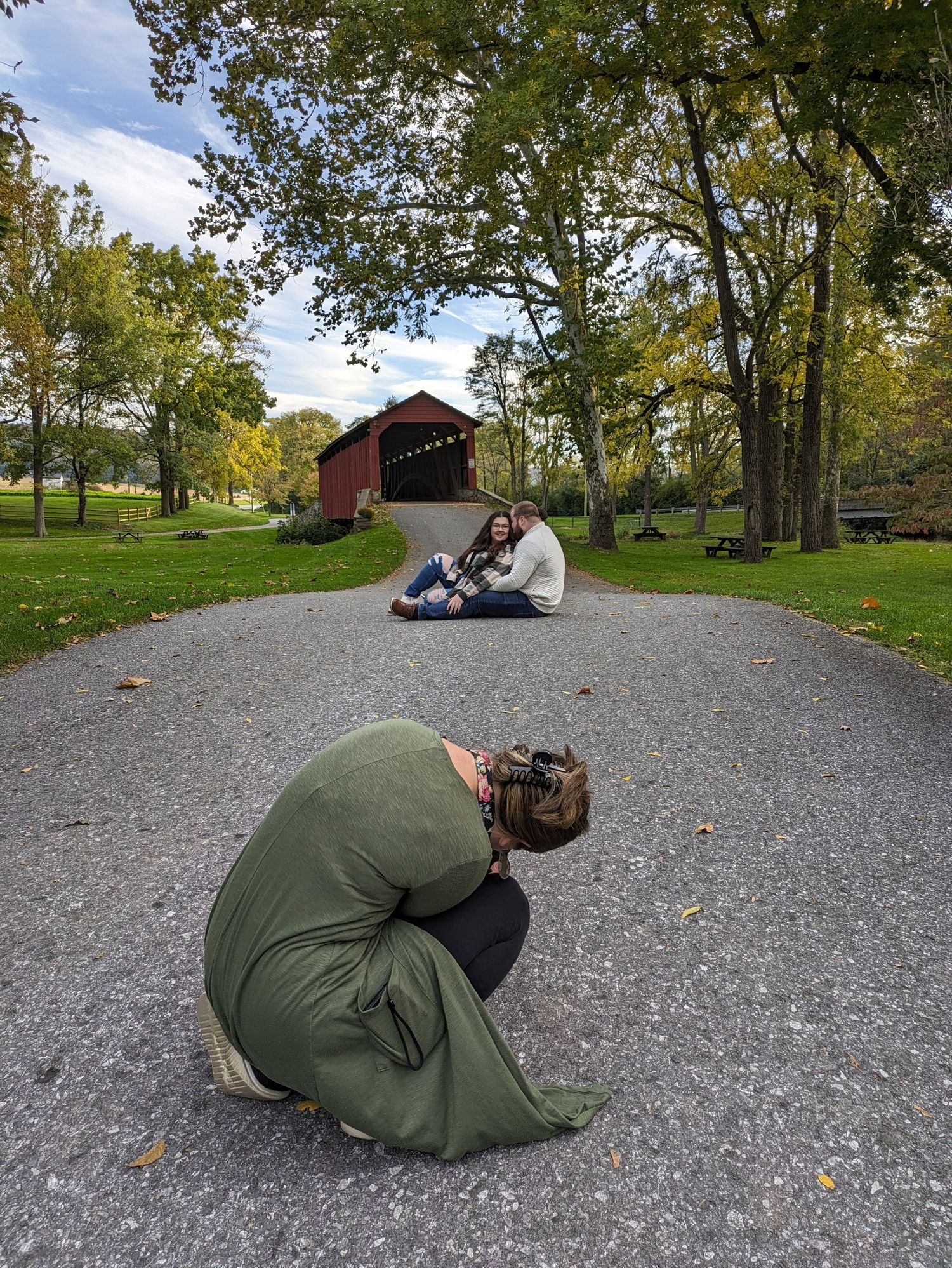 Multiple photographers lay on ground to capture shots of covered bridge in autumn setting.