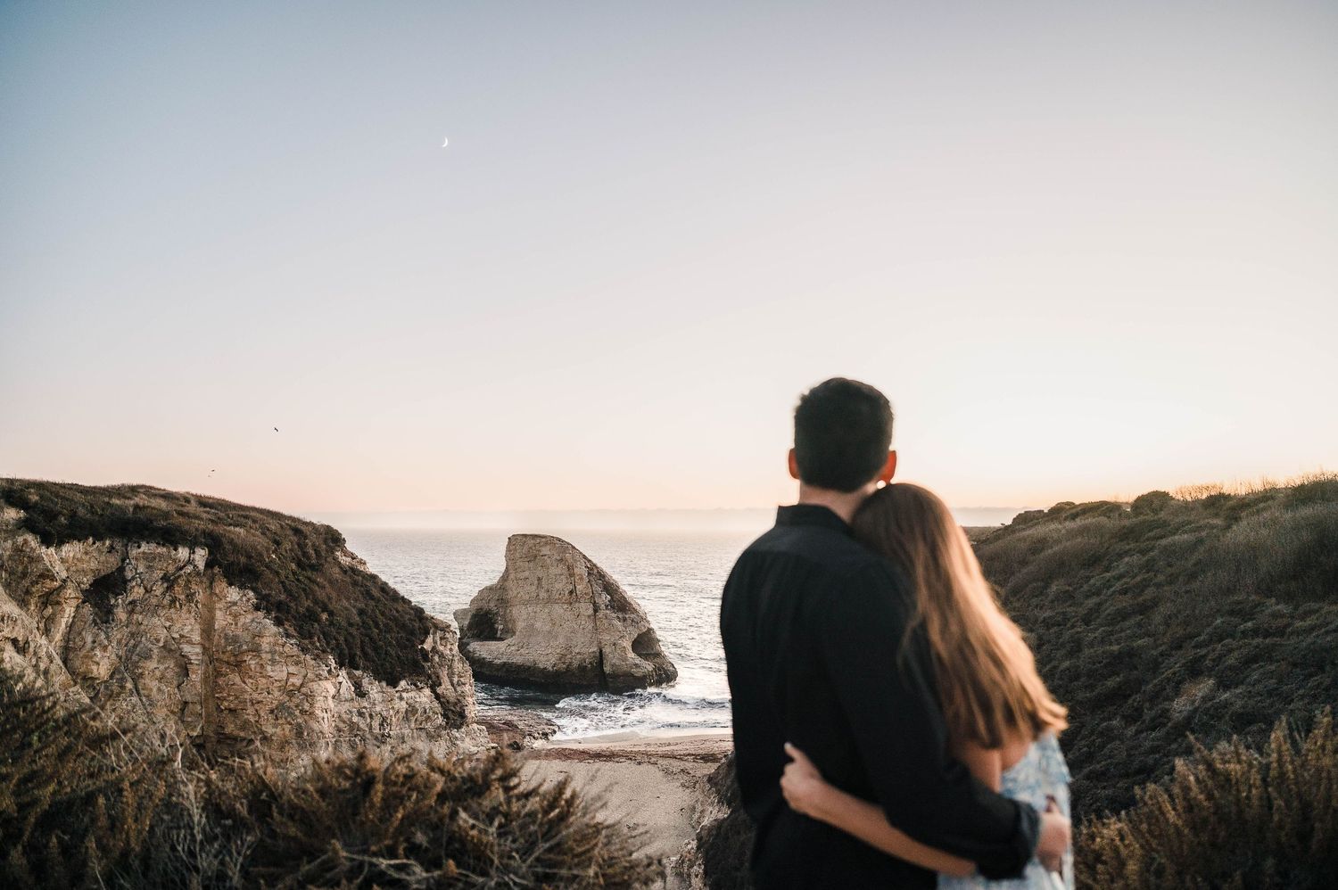 Couple enjoying a peaceful moment overlooking a rocky beach at dusk.