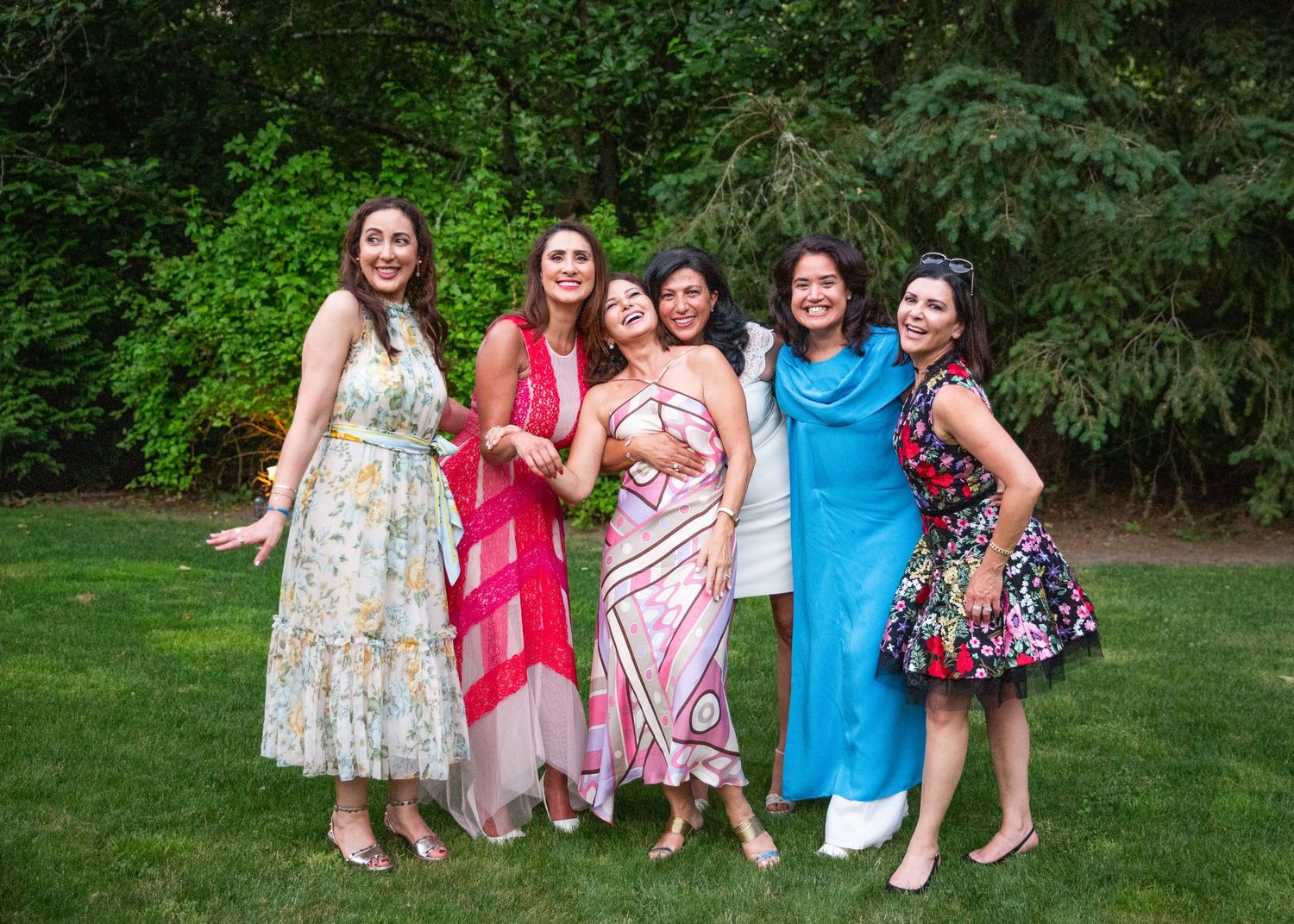 A group in colorful summer dresses poses together on a green lawn during an outdoor gathering.
