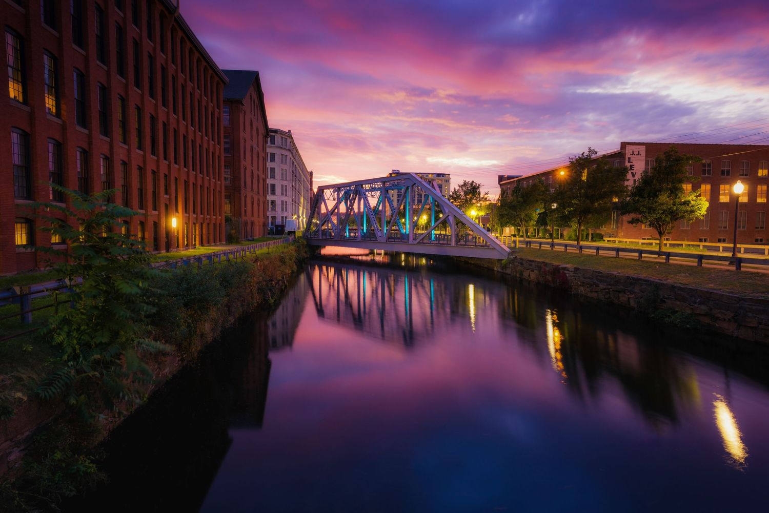 Historic brick buildings line the Hamburg canal at sunset as vibrant purple and pink clouds reflect in the calm water.