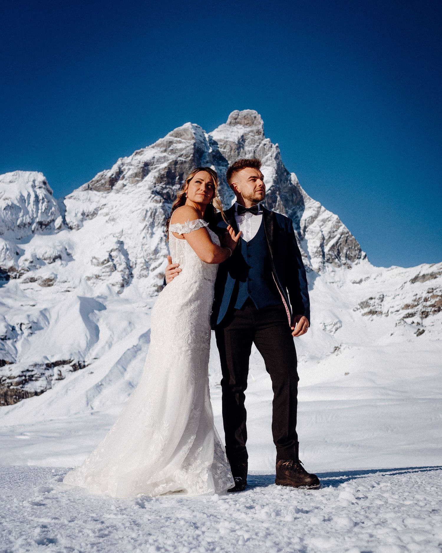 Wedding couple standing in snow with majestic mountain peaks in the background.