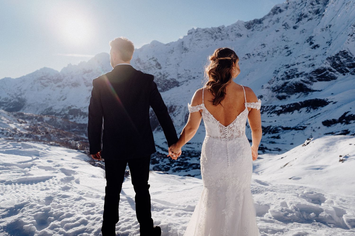 Couple holding hands while facing snowy mountain landscape on their wedding day.