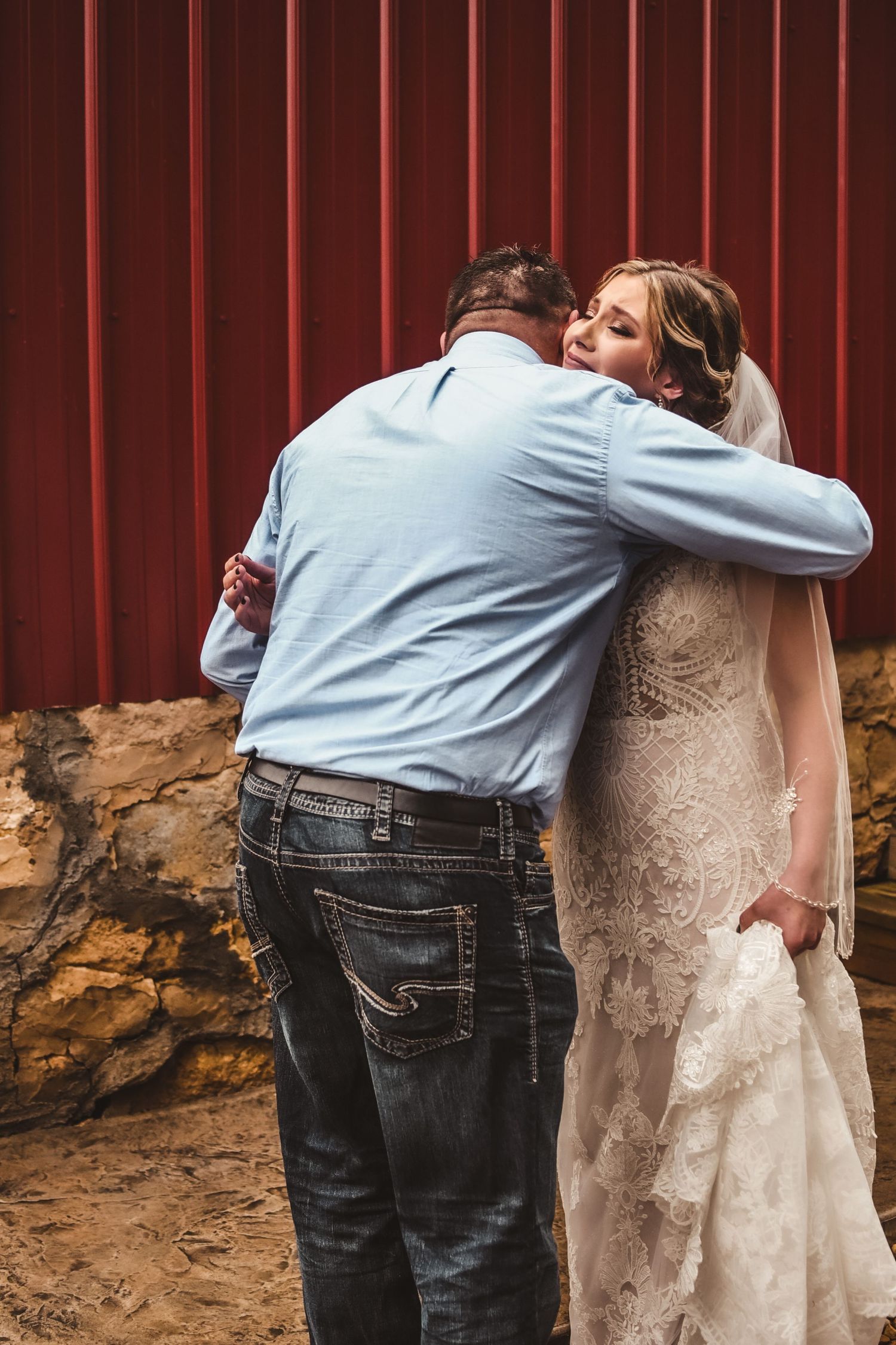 A tender embrace between newlyweds against a rustic red barn wall during their wedding celebration.