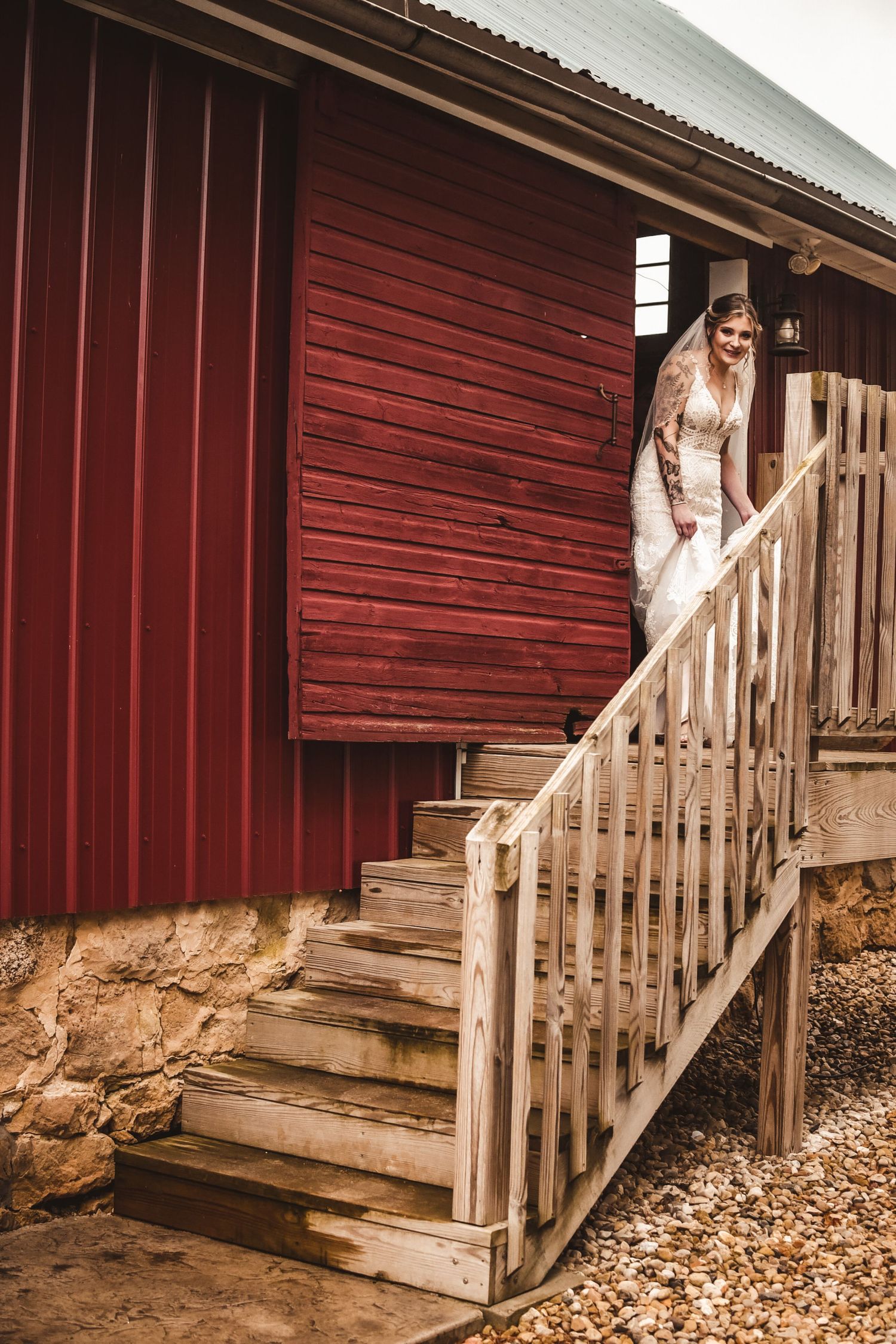 White wedding dress descending wooden stairs of red barn building.