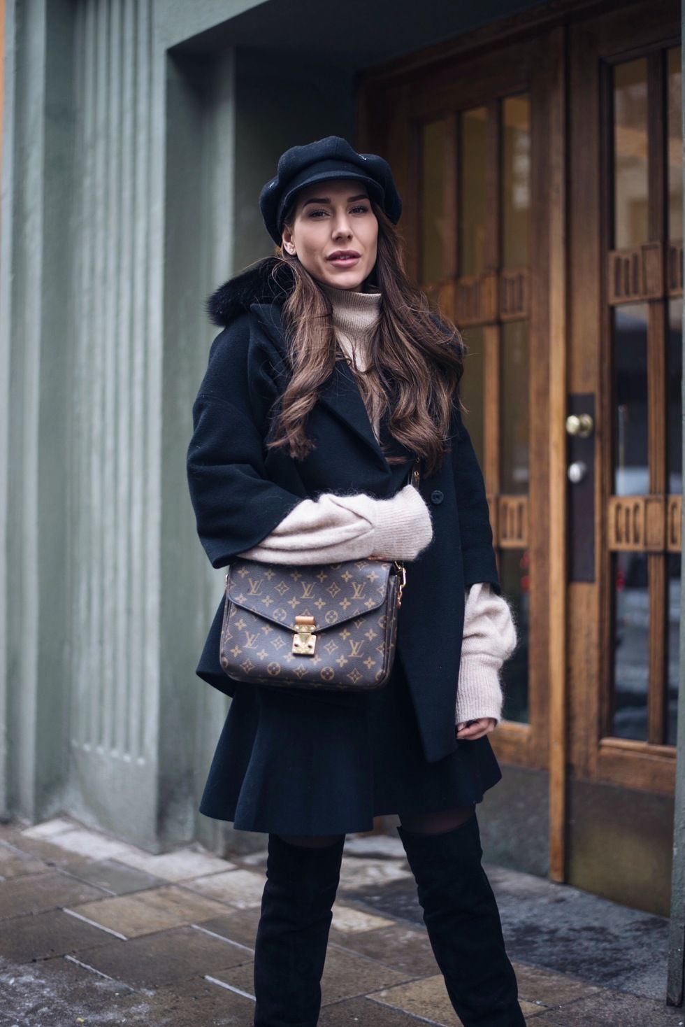 Winter street style with black coat, baker boy cap and designer handbag.