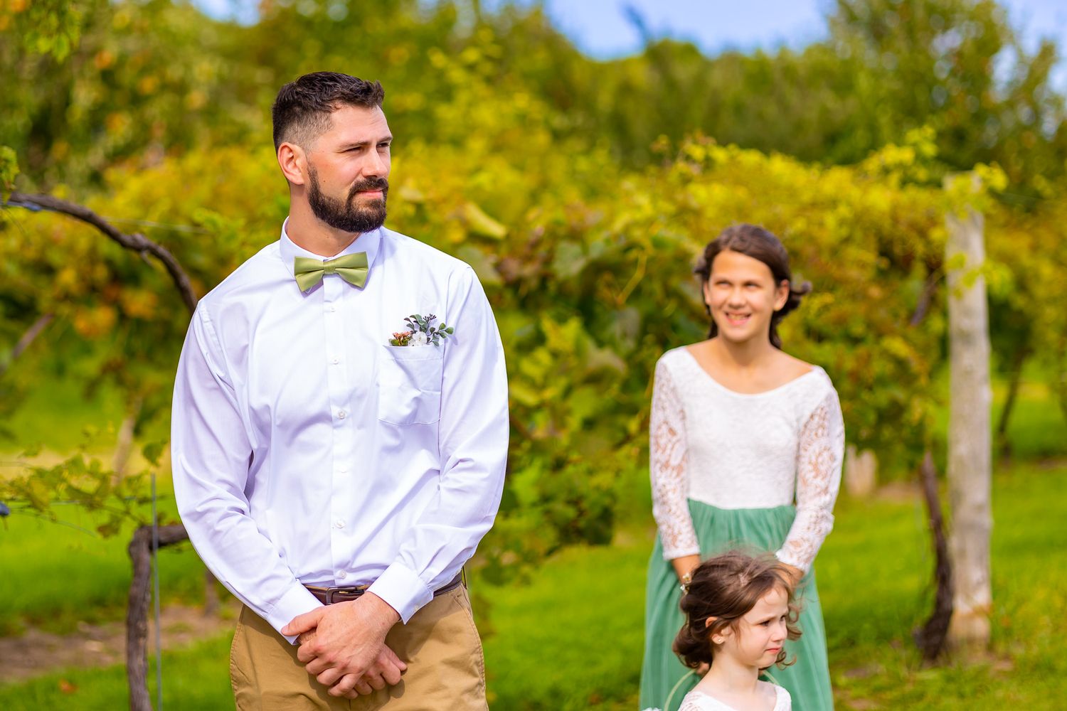 A small wedding party stands together outdoors on a sunny autumn day.