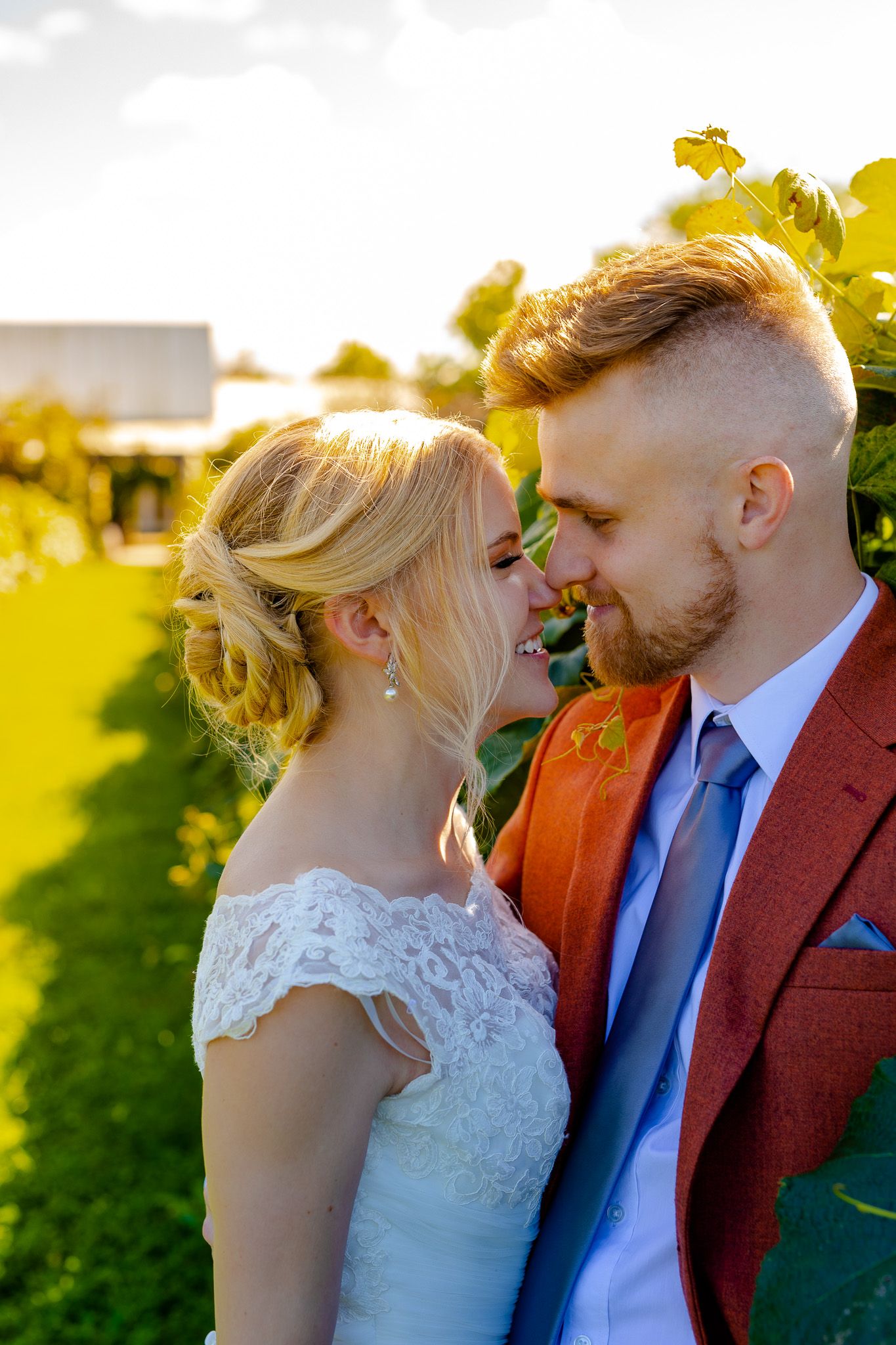 A romantic wedding portrait of a couple in front of sun-lit vineyard.