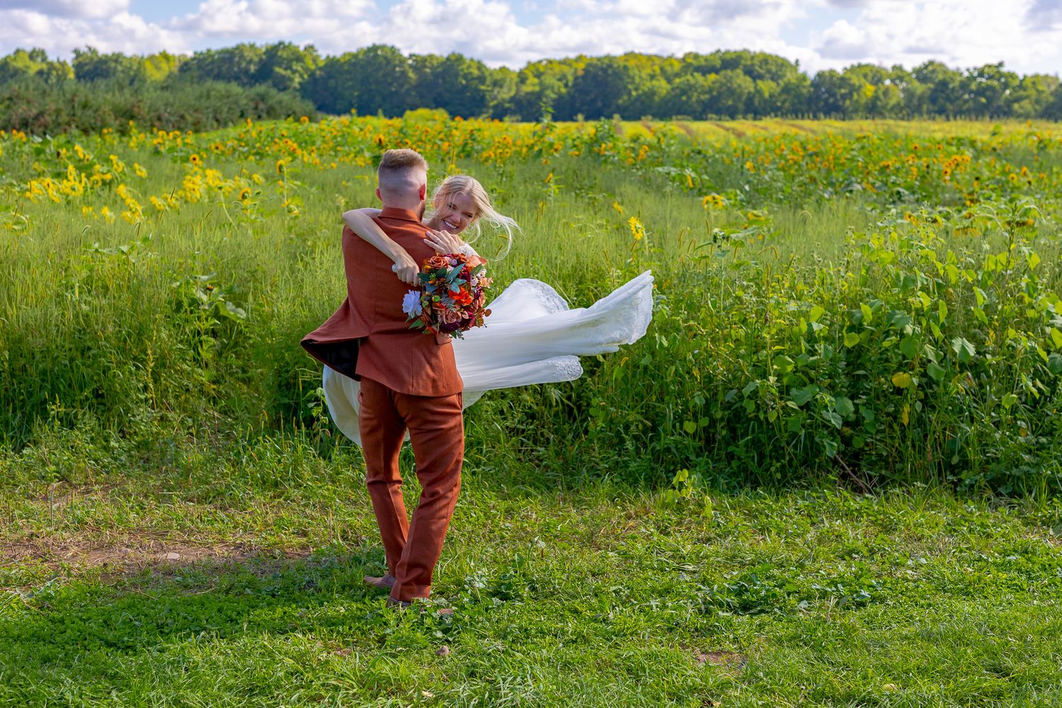 A couple embracing in a vibrant yellow wildflower field under blue skies.