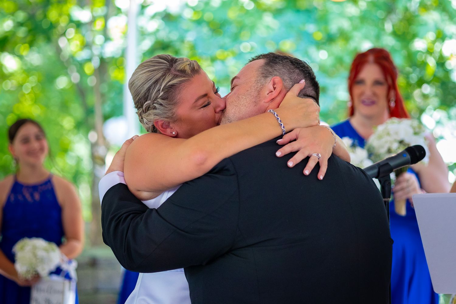 A tender embrace during an outdoor wedding ceremony with guests in blue dresses.